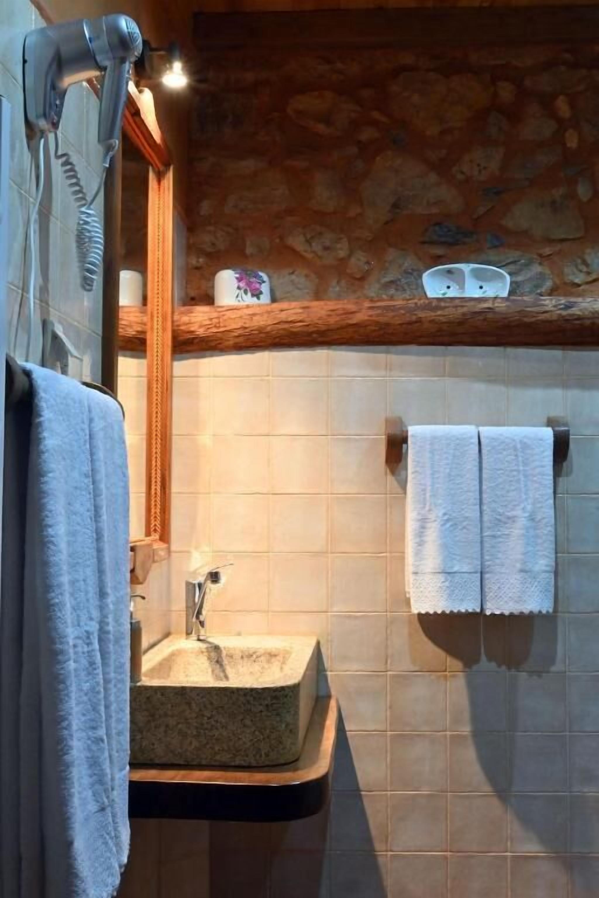 Une salle de bain avec un mur en pierre, une étagère en bois où sont rangés les articles de toilette, un lavabo et un porte-serviettes.