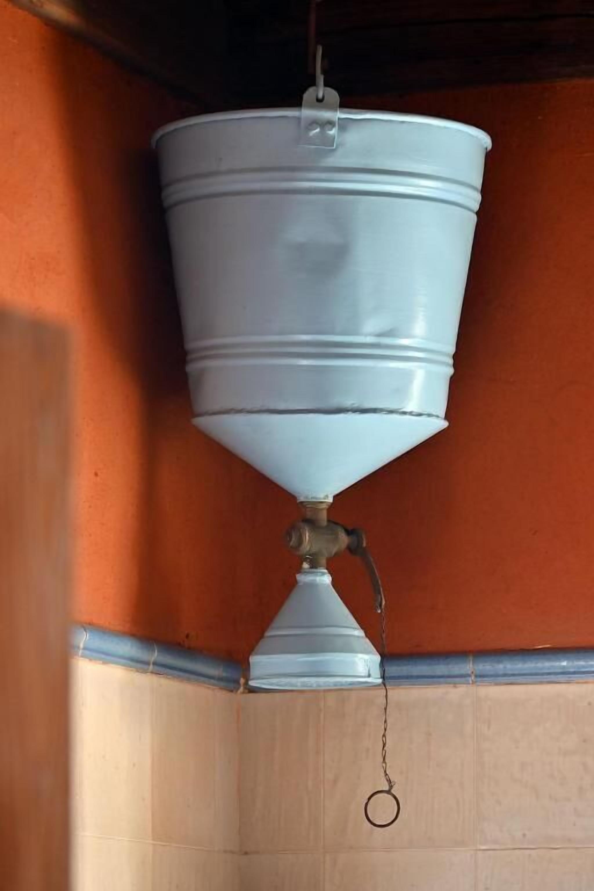 A white industrial-style water dispenser mounted on a wall with a metal pipe and a chain.