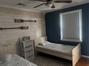 A bedroom with a single bed, a dresser, a window with blinds, a ceiling fan, and wooden wall paneling.