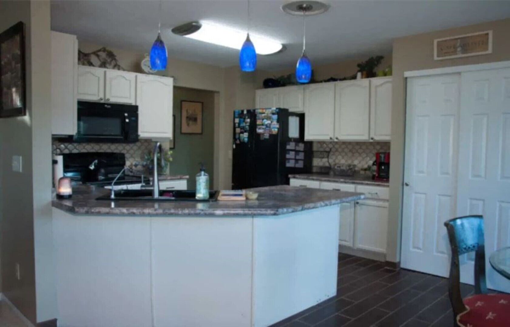 A kitchen with white cabinets, a black refrigerator, a microwave, and blue pendant lights.
