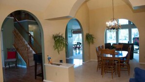 A spacious living area with a dining table, chairs, a chandelier, and a staircase. - Fairway Haven at The Falls – Golf, Shops, Dining! 10-12 Mins. Equestrian Center (O'Fallon)