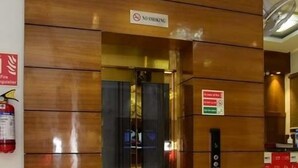 A hotel entrance with a wooden facade, a fire extinguisher, a no-smoking sign, and a digital elevator control panel. - Hotel R.K. Regency (Rohtak)