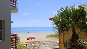 Vista de la piscina con una playa al fondo, una palmera y un paraguas rojo.