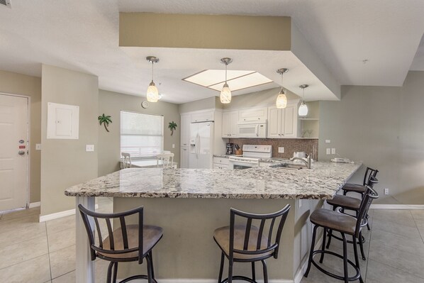 A kitchen with a large island, bar stools, a microwave, and a stove. - Luxury Updated Beach Condo - Crimson #104 (Madeira Beach)