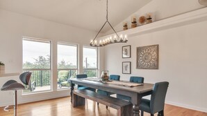 Un espace repas comprenant une grande table, des bancs et des chaises. De grandes fenêtres offrent une vue sur l’extérieur.
