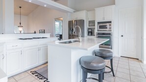 Une cuisine moderne avec des meubles blancs, des appareils en acier inoxydable et un îlot central doté de tabourets.