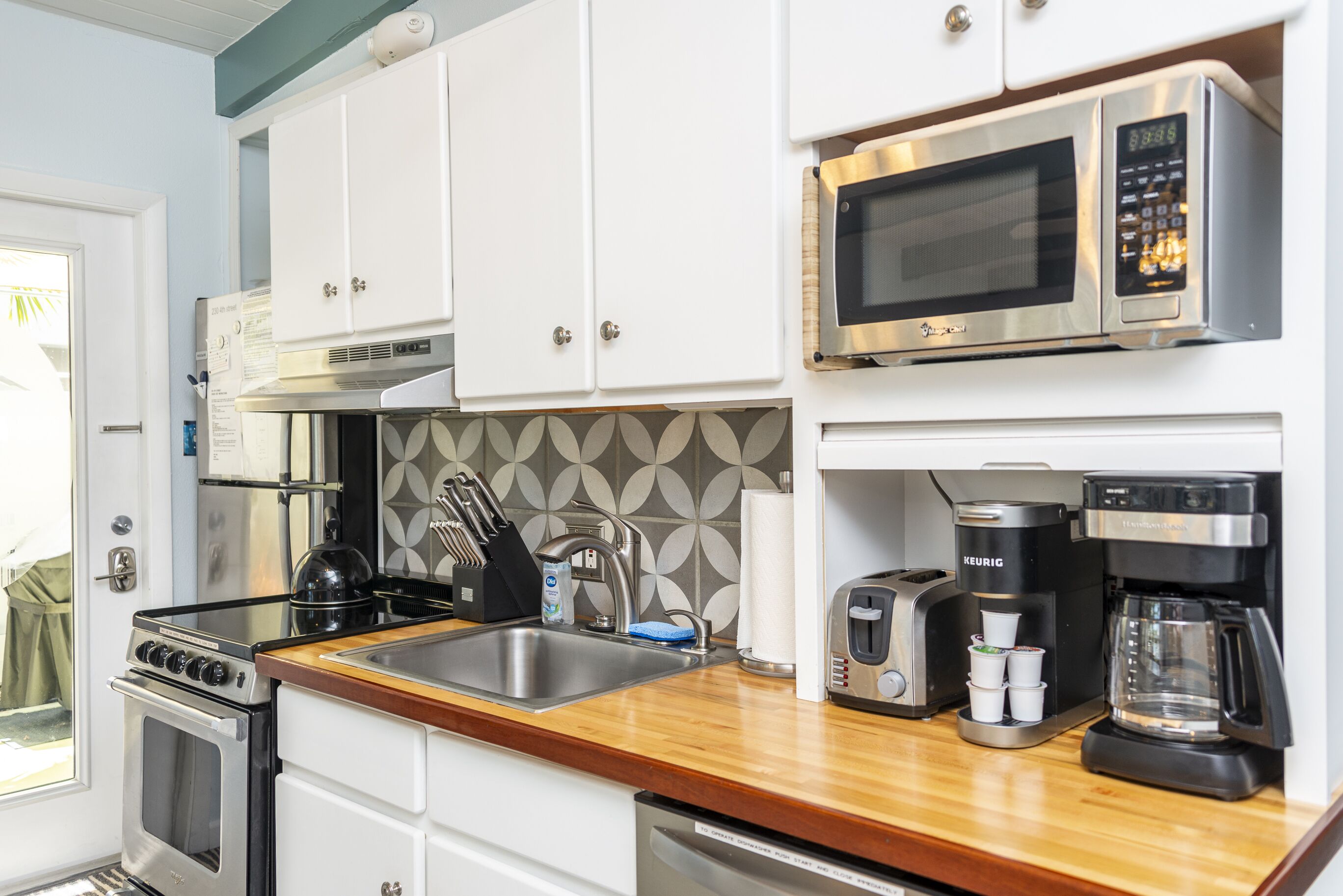 Una cocina moderna con armarios blancos, electrodomésticos de acero inoxidable, microondas, tostadora y cafetera.