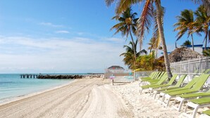 A beach with a row of green lounge chairs, a thatched-roof structure, and a pier extending into the water. - Razz's Retreat at KCB! (Key Colony Beach)