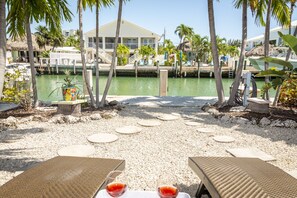 A beachfront patio with round tables and chairs, a view of the marina, and palm trees.