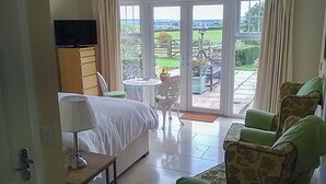 A bedroom with a bed, a TV, a small table, and a chair. There is a sliding glass door leading to an outdoor patio with a table and chairs. - 1 bedroom accommodation in Todenham, near Moreton-in-Marsh (Todenham, near Moreton-in-Marsh)