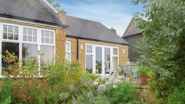 A residential house with a garden, a patio with chairs, and a stone wall. - 1 bedroom accommodation in Todenham, near Moreton-in-Marsh (Todenham, near Moreton-in-Marsh)