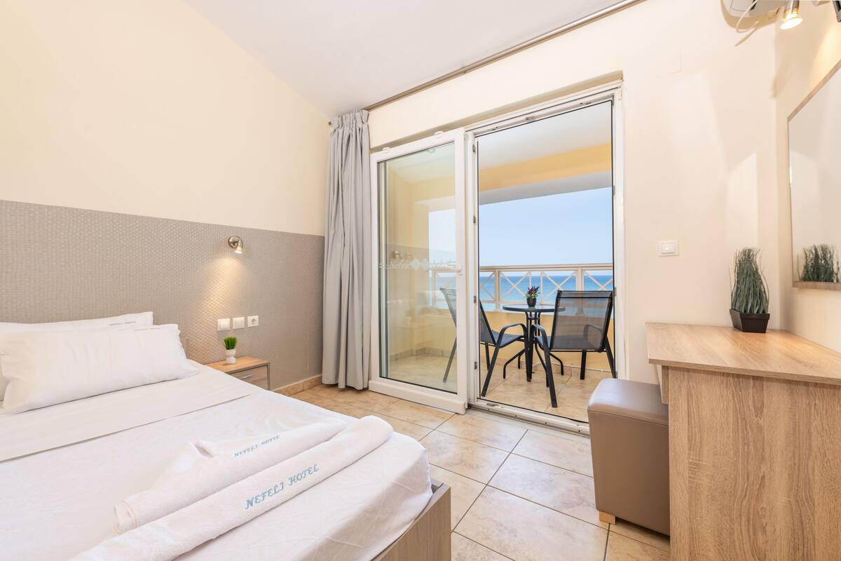 A hotel room with a bed, a desk, a chair, a small table, and a balcony with a view.