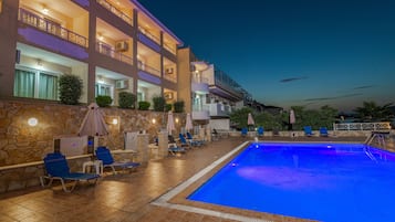 Un hotel con piscina, sillas de descanso y sombrillas.