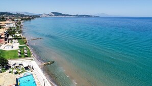 Hotel à beira-mar com piscina, acesso direto à praia e vista para o mar e montanhas ao longe.