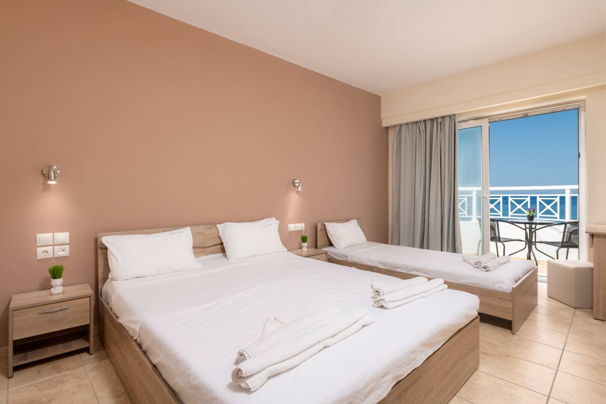 A hotel room with two beds, a balcony with a table and chairs, and a view of the sea.