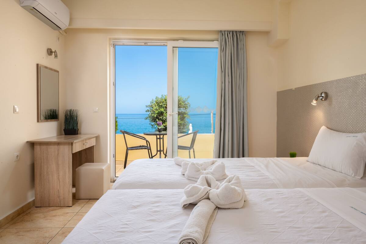 A hotel room with a bed, a desk, a chair, and a view of the sea.