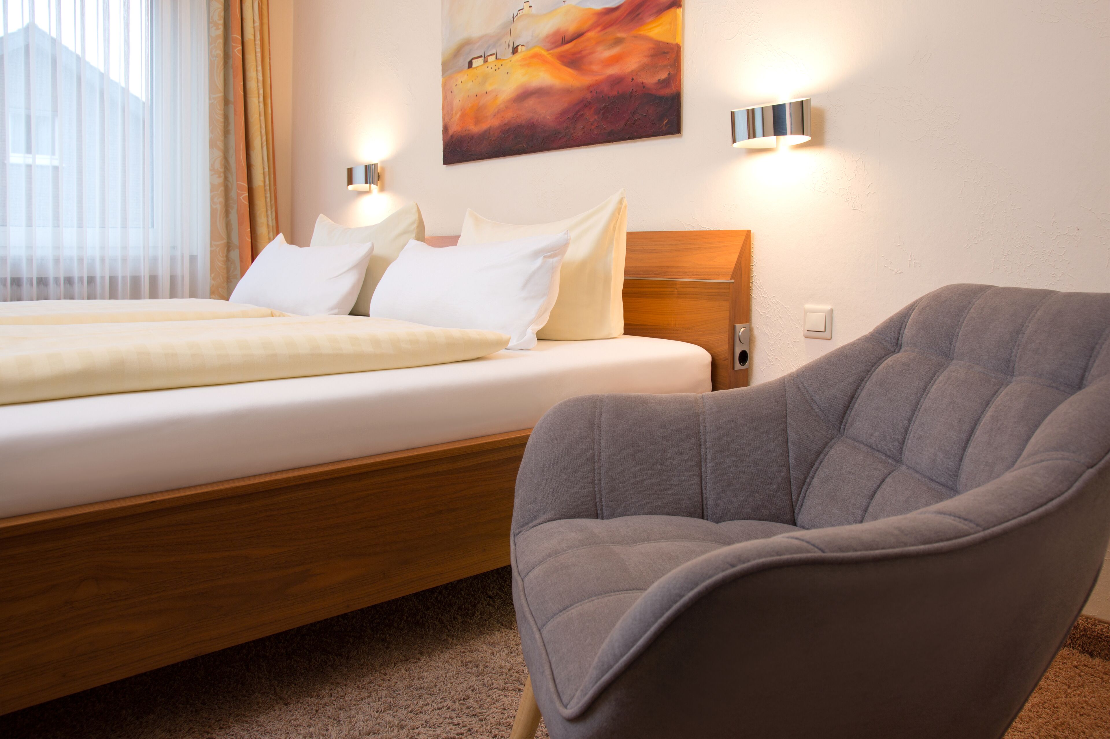 Una habitación de hotel con una cama, un sillón gris y un cuadro en la pared.