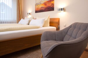Una habitación de hotel con una cama, un sillón gris y un cuadro en la pared.