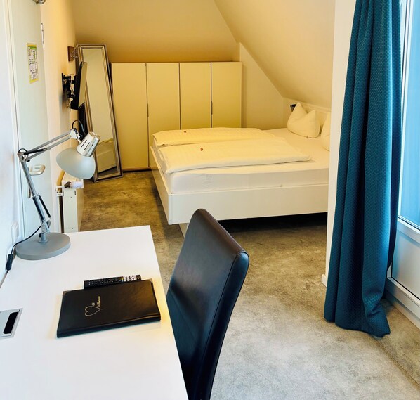 A small, neatly arranged bedroom with a single bed, a desk with a lamp, a chair, and a window with curtains. - Parkhotel Lippstadt (Lippstadt)
