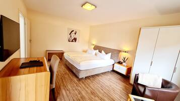 A hotel room with a bed, bedside table, lamp, wardrobe, desk, chair, and a TV.