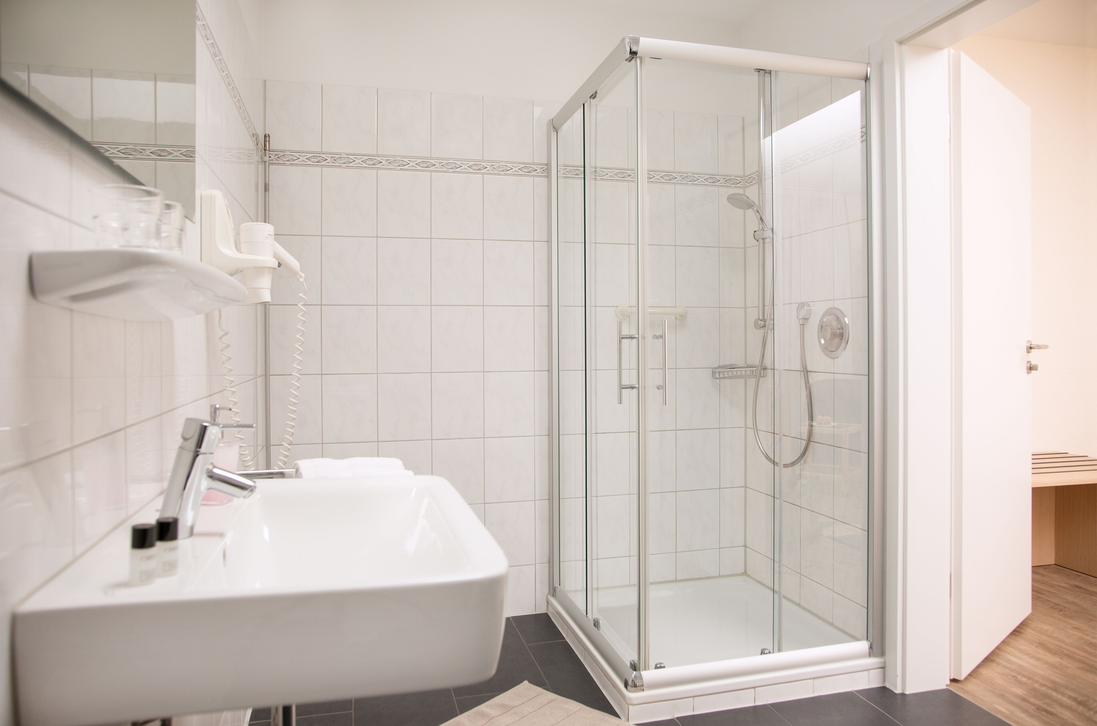 Un baño moderno con ducha vidriada, un lavabo blanco y un espejo.