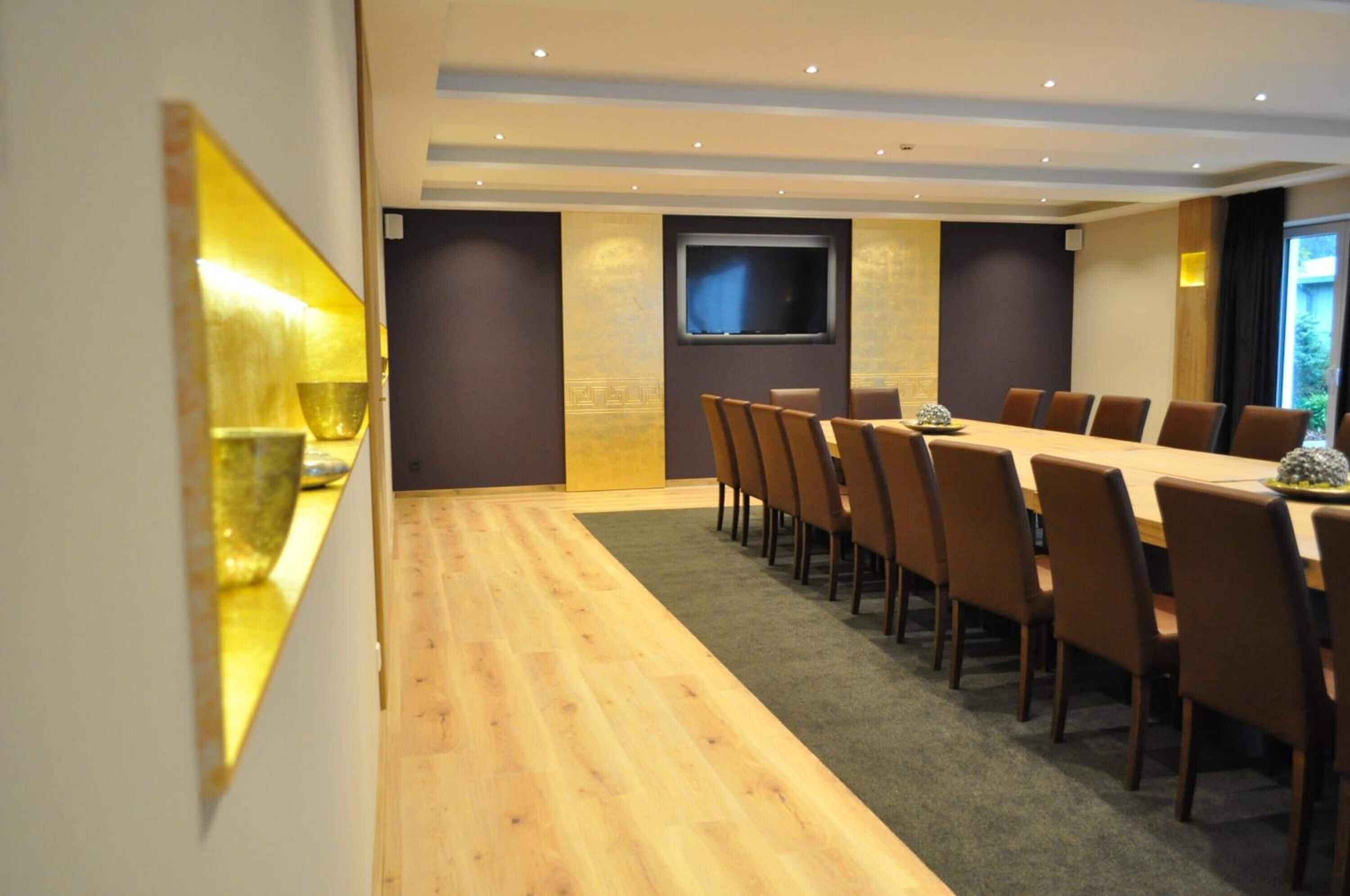 Ein Konferenzraum mit langem Tisch, Stühlen, einem Fernseher und einem Wandbild.