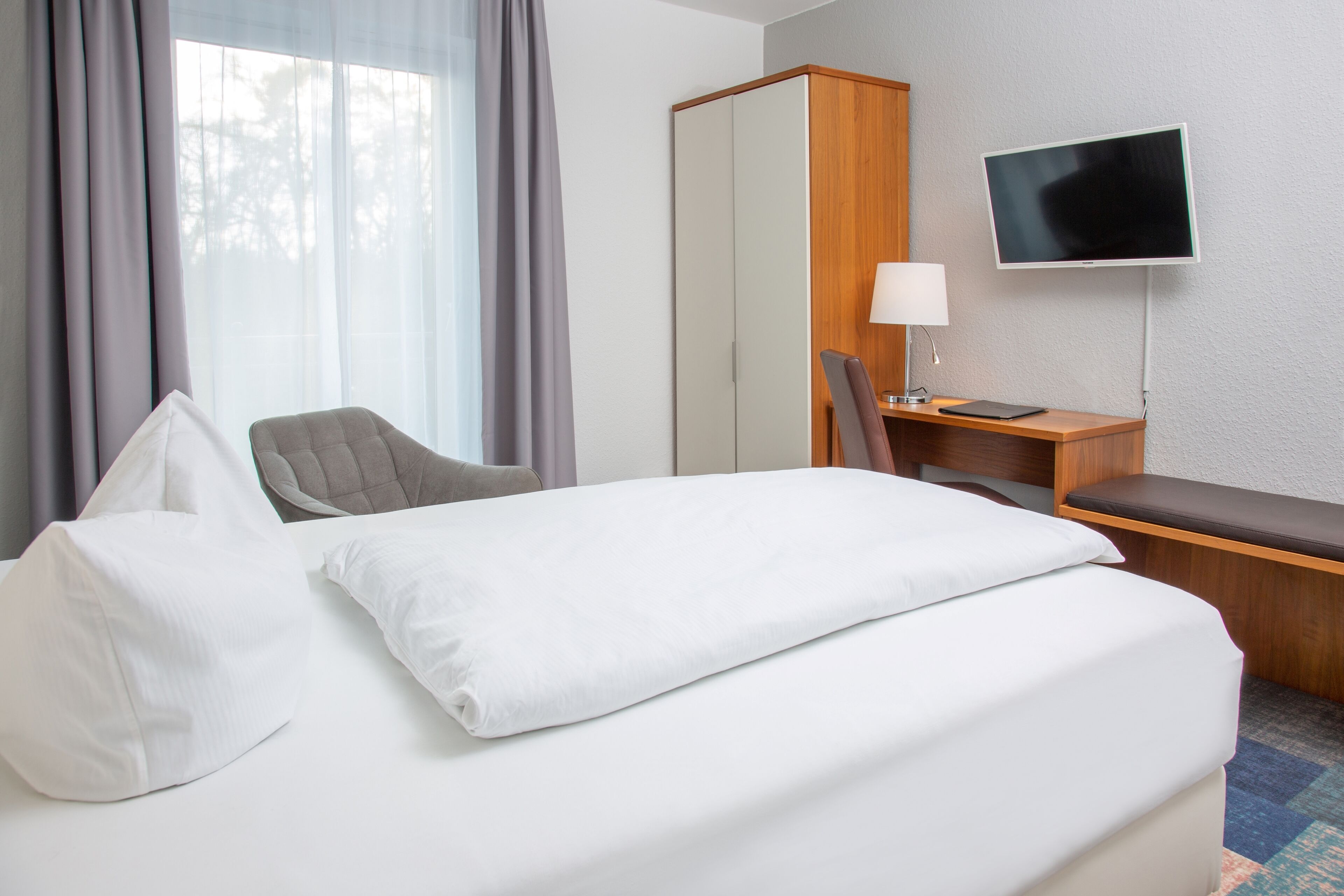 Ein Hotelzimmer mit Bett, Schreibtisch, Stuhl, Fernseher und Kleiderschrank.