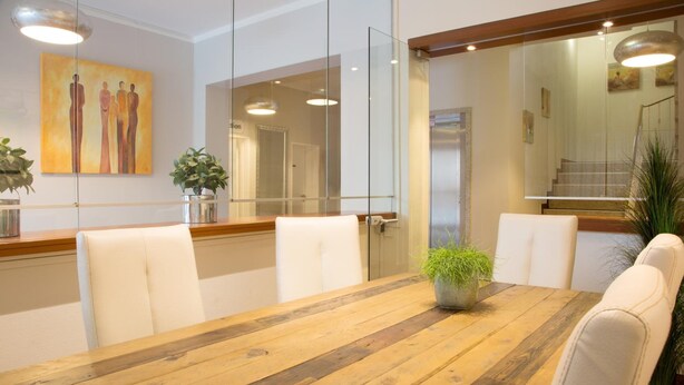 Una sala conferenze con un tavolo di legno, sedie bianche, pareti divisorie in vetro e un quadro appeso al muro.