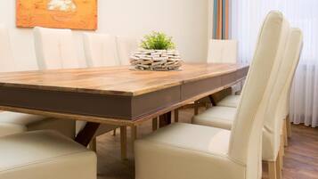 A modern dining room with a wooden table, white upholstered chairs, a potted plant, and a large abstract painting on the wall.