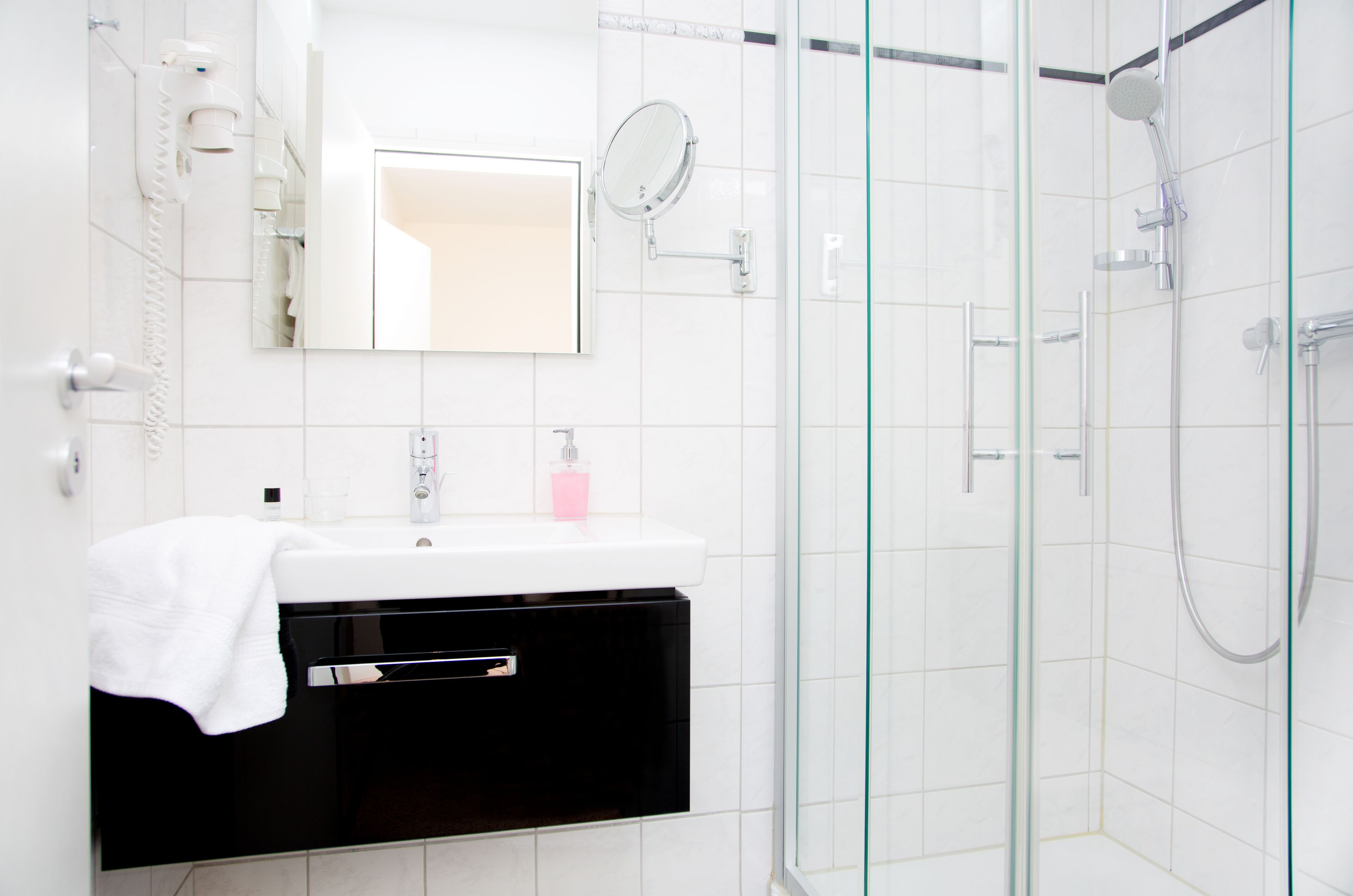 Un baño moderno con cabina de ducha de vidrio, un lavamanos blanco con un espejo encima y un mueble negro debajo.