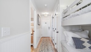 Un couloir étroit, avec un lit superposé sur le côté droit, une porte au fond et un tapis à motifs sur le sol.