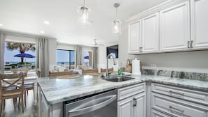 A modern kitchen with white cabinetry, a marble countertop, and a dishwasher. - Latitude 14 - NEW OWNER! NEW LOOK! Spectacular ocean views! 1BD/2BA. Sleeps 6 (Panama City Beach)