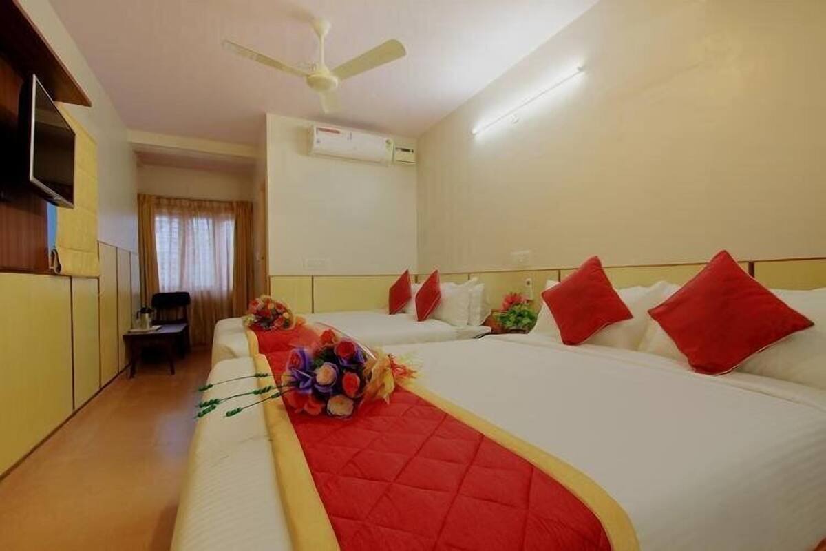 A hotel room with two beds, a flat-screen TV, an air conditioning unit, and a ceiling fan.