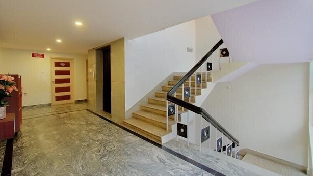 Un hall d’hôtel avec un sol en marbre, un escalier doté d’une rampe noire et une porte ornée d’une enseigne rouge.