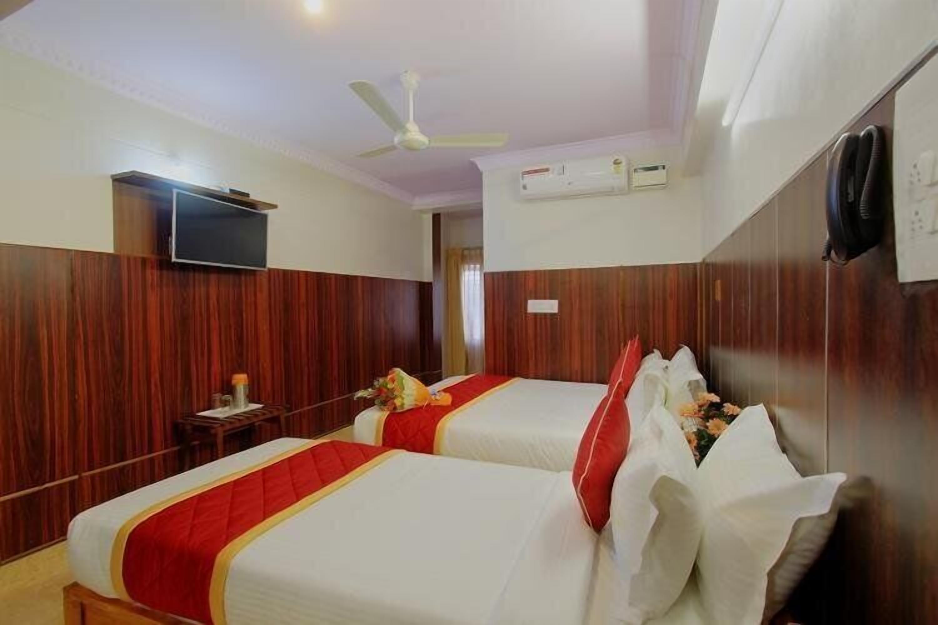 A hotel room with two beds, a television, an air conditioning unit, and a ceiling fan.