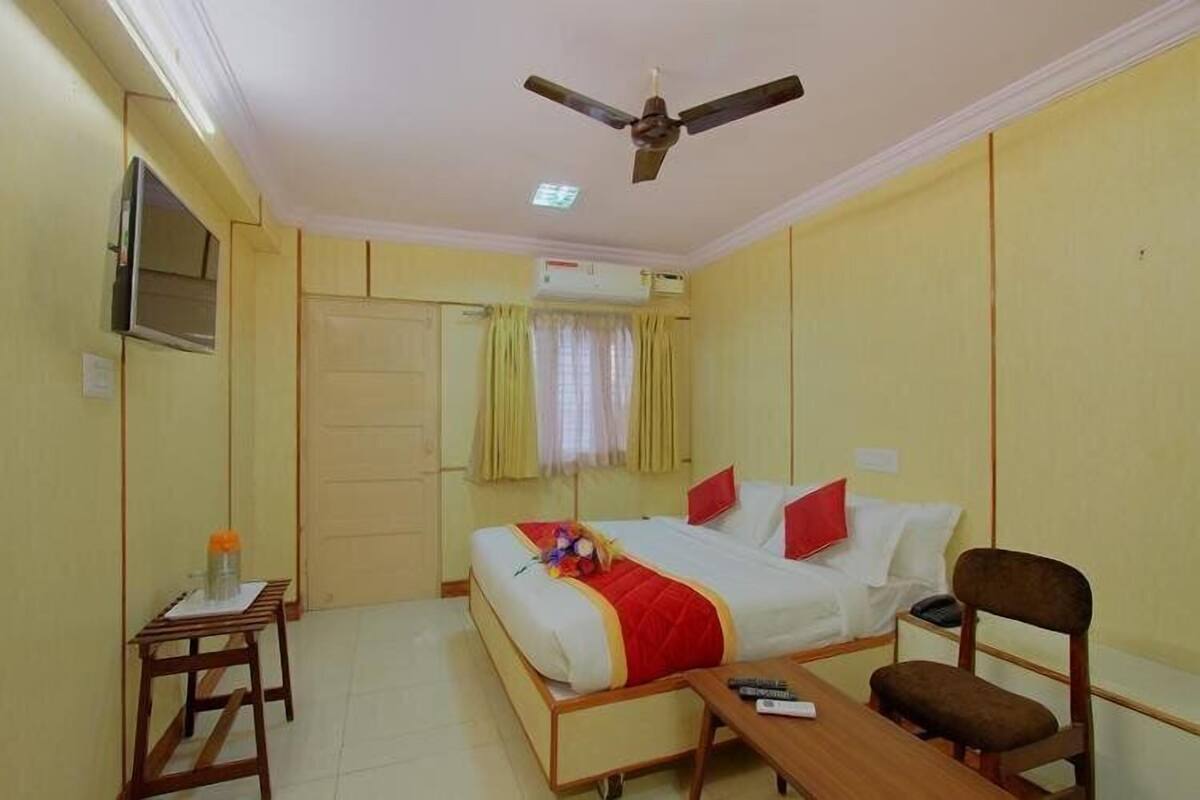 A hotel room with a bed, a desk, a chair, a ceiling fan, and an air conditioning unit.