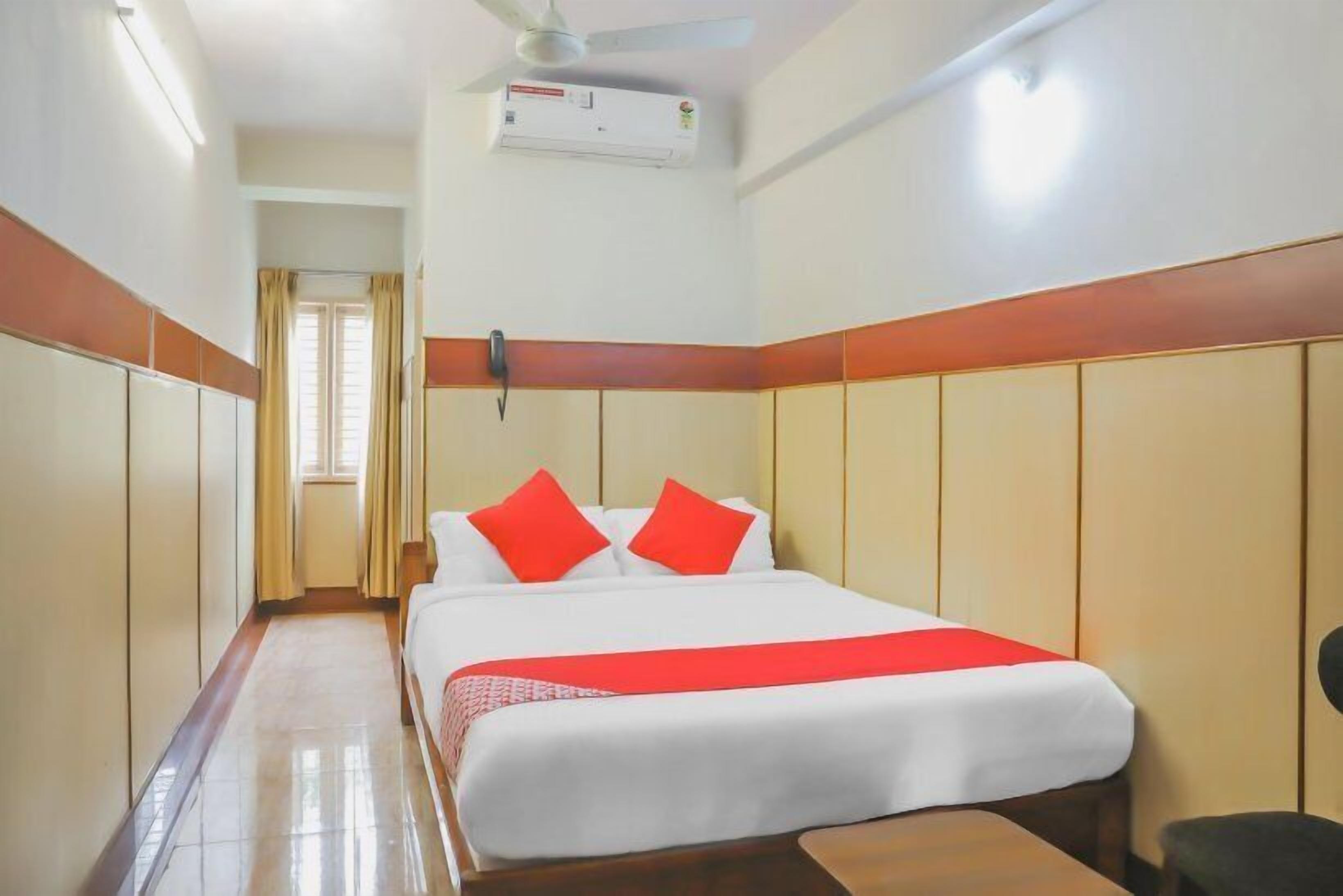 A hotel room with a bed, a ceiling fan, an air conditioning unit, and a window with curtains.