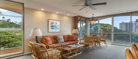 A spacious room with a large window, a ceiling fan, a sofa set, and a dining table.