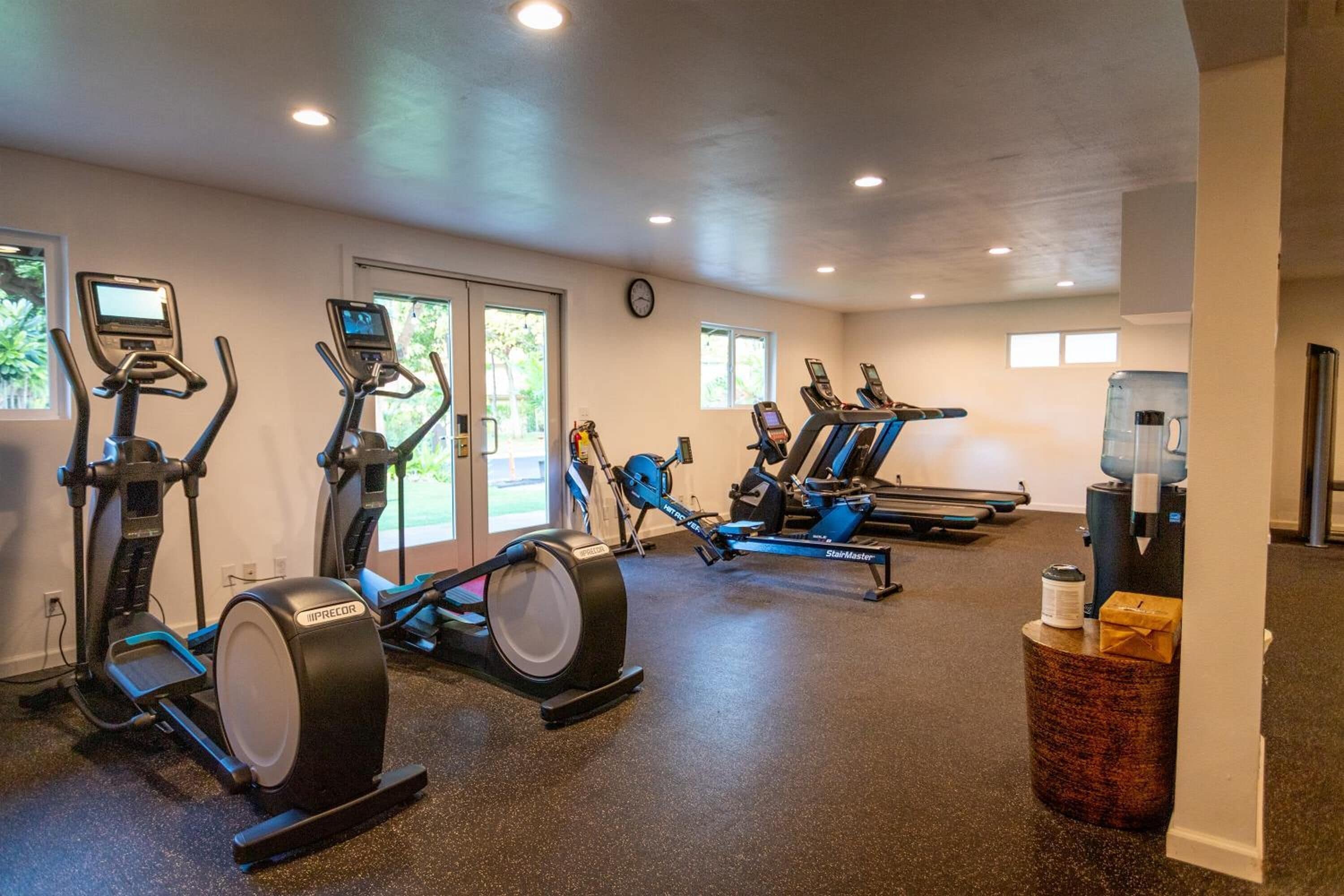 Une salle de sport équipée de divers appareils de cardio, notamment des tapis de course et des vélos elliptiques, ainsi qu’un distributeur d’eau.