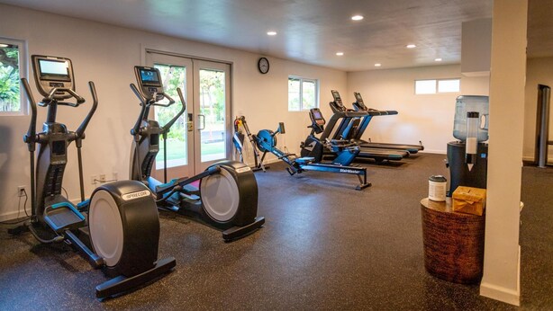 Un gimnasio con equipos de cardio variados, incluyendo cintas de correr y elípticas, y un dispensador de agua.