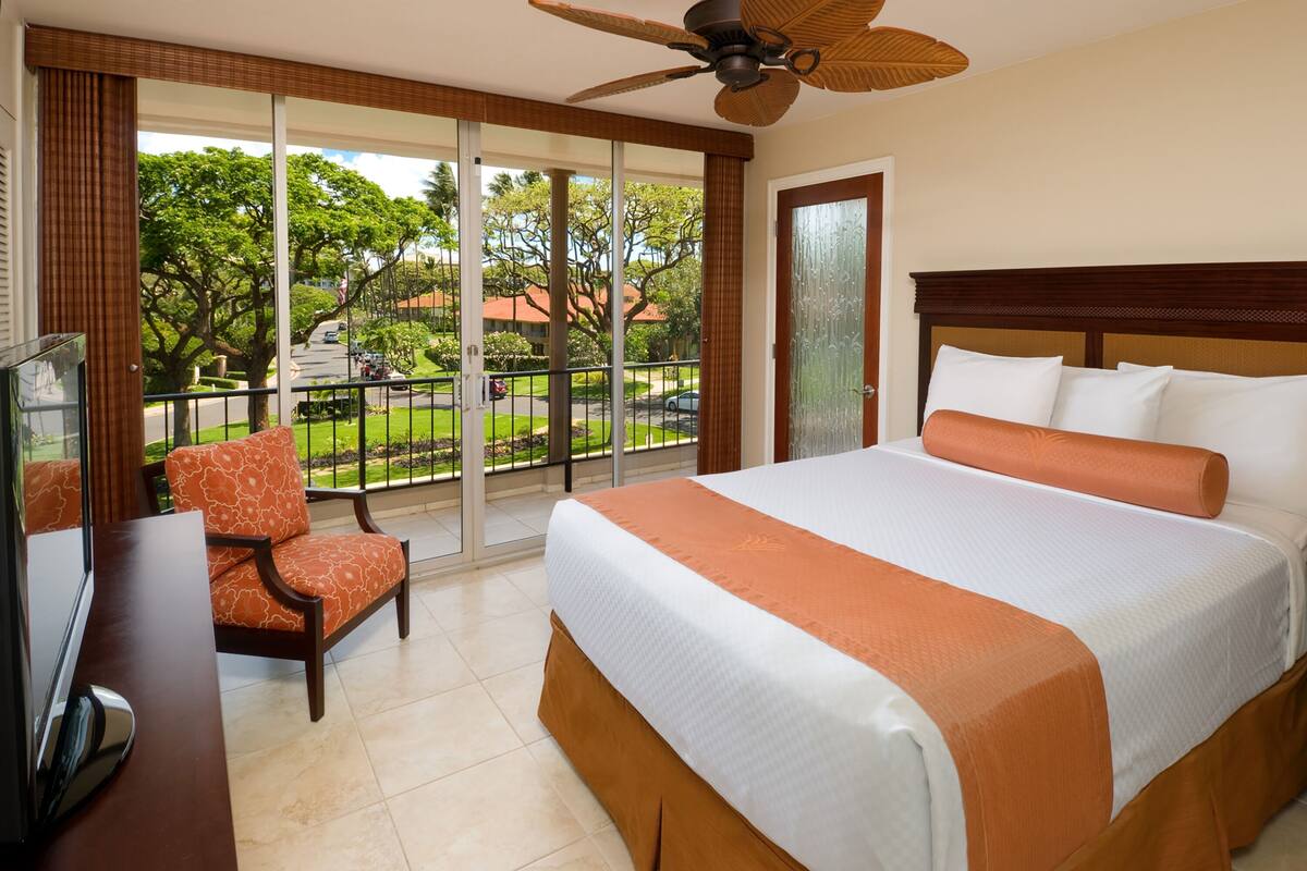 Habitación de hotel con una cama grande, televisión, una silla y balcón con vistas al exterior.