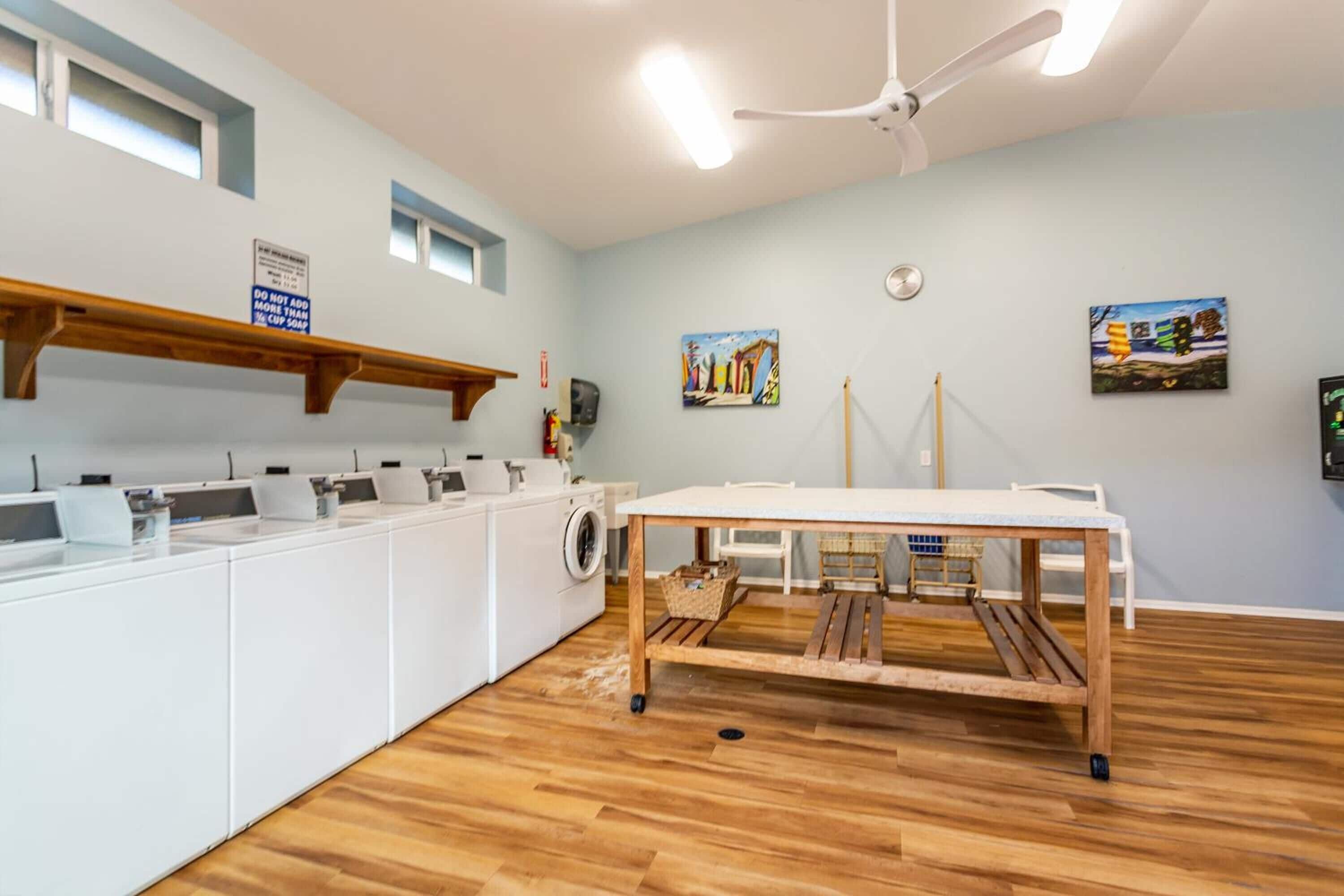A laundry room with a wooden table, washing machines, and a ceiling fan.