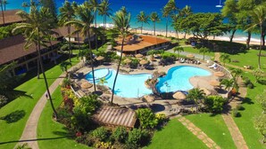 Un resort con piscina central, palmeras y vista al mar.