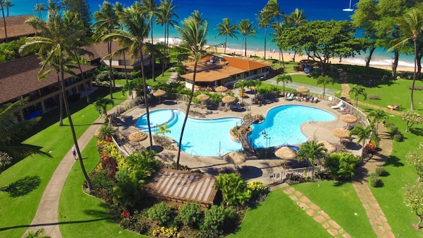 A resort with a central swimming pool, palm trees, and a beach view.