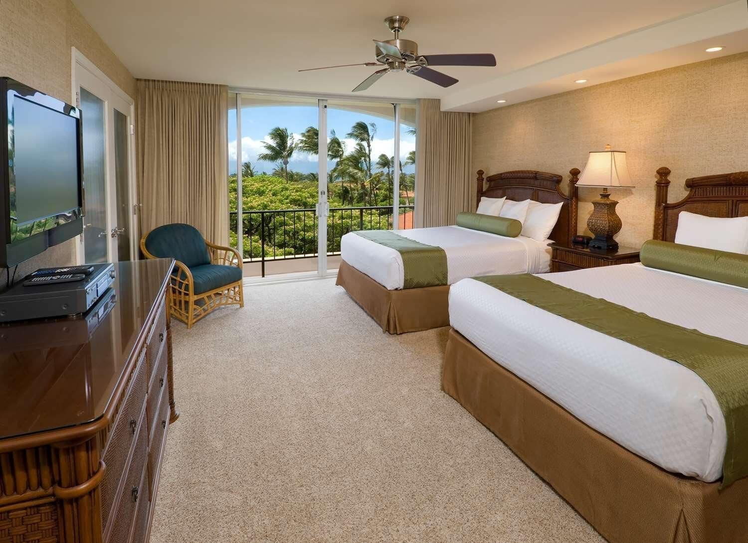A hotel room with two beds, a television, a chair, and a balcony with a view of palm trees.
