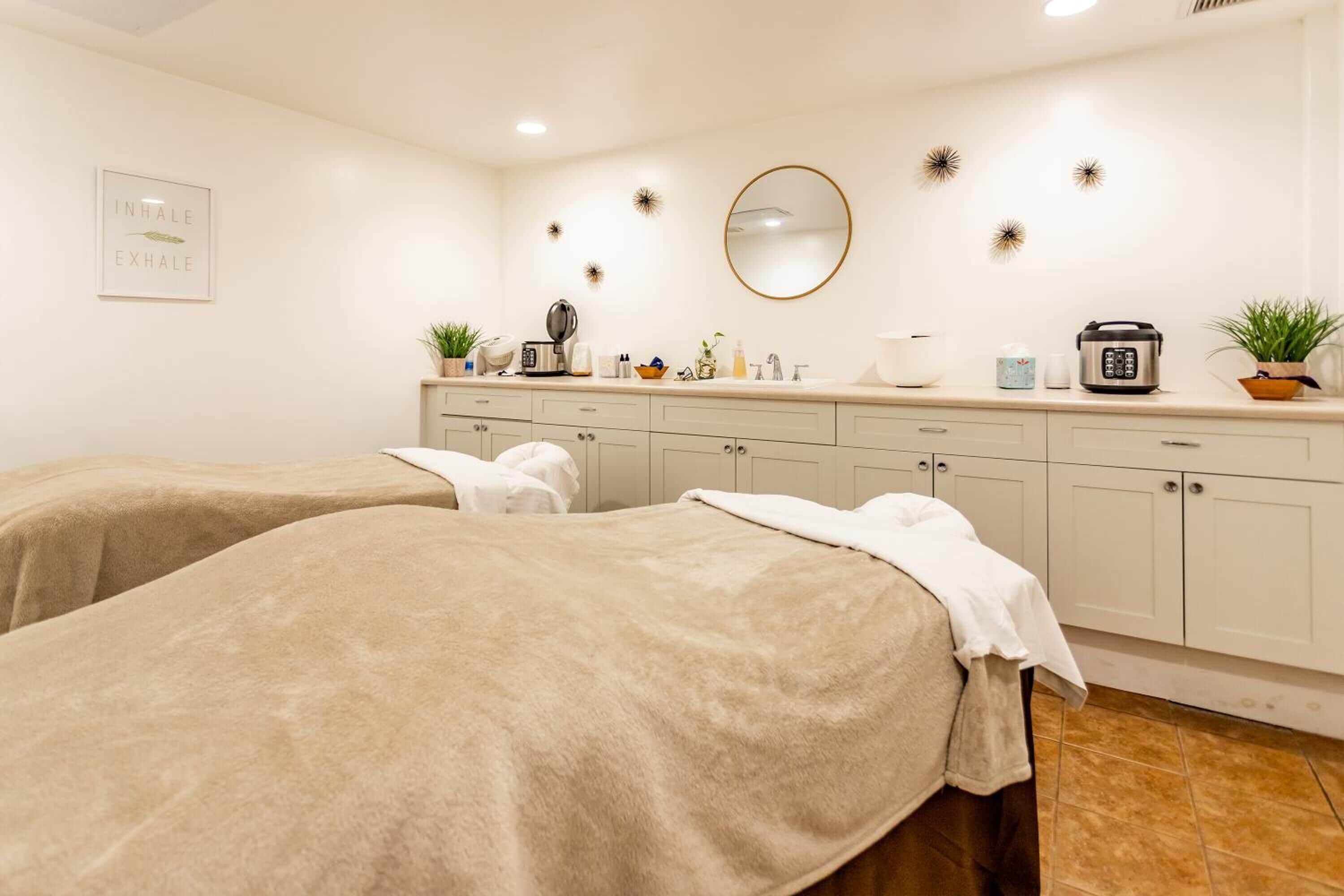 A spa room with two massage beds, a sink, and a mirror.