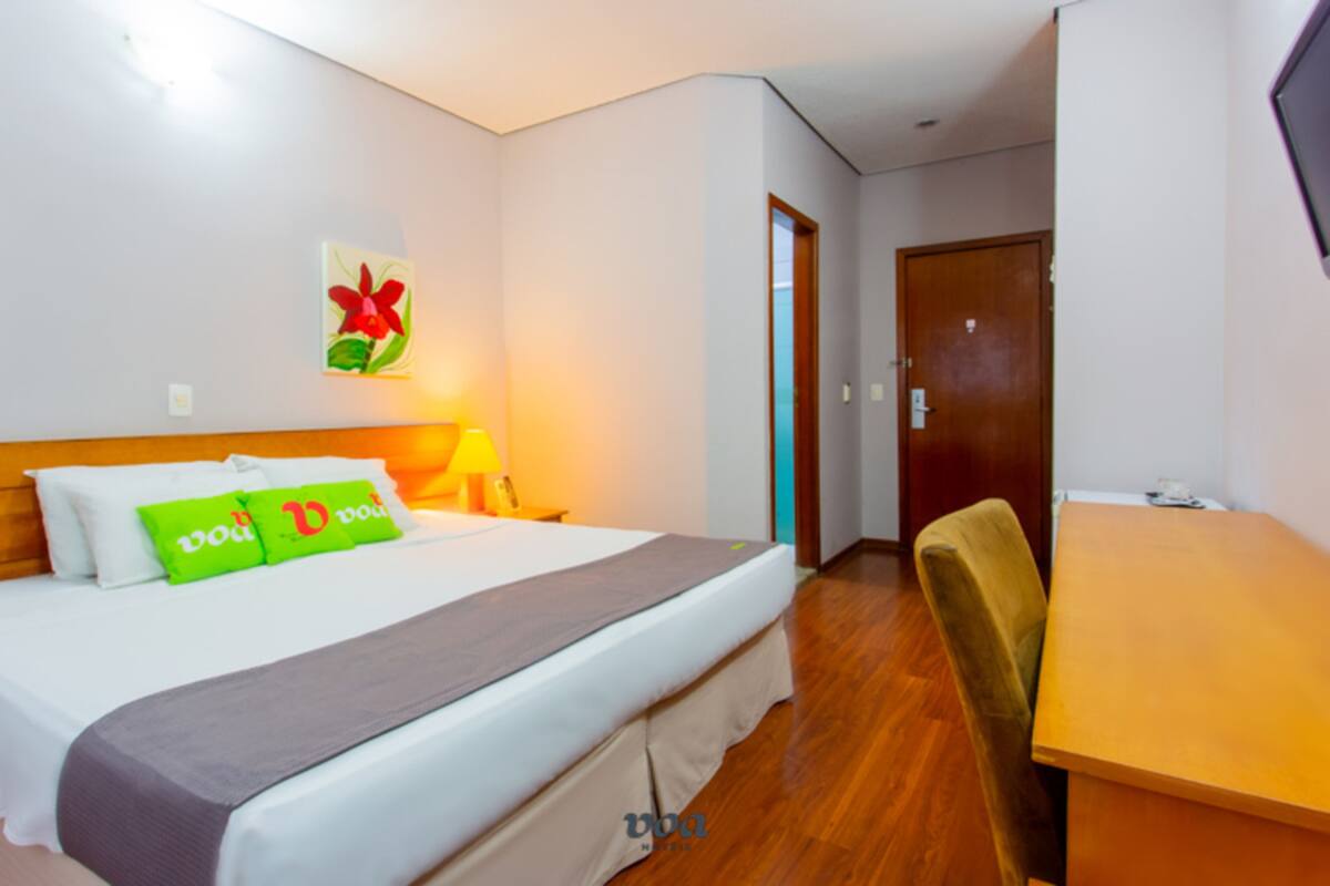 A hotel room with a bed, a desk, and a door.
