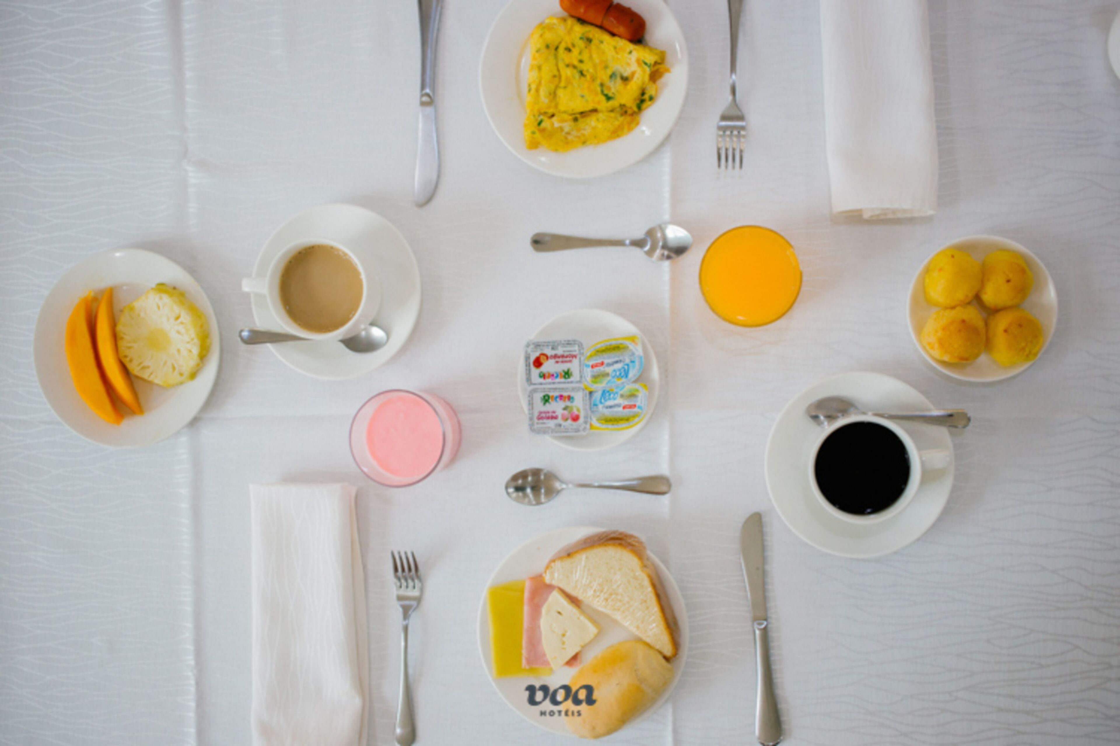 Une table de petit-déjeuner avec des assiettes remplies de nourriture, des tasses de café et une variété de condiments.