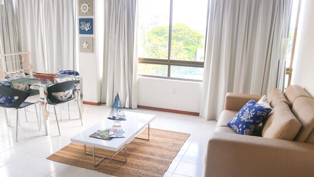 Un soggiorno con un tavolo in vetro, un divano color beige e vista sul verde.