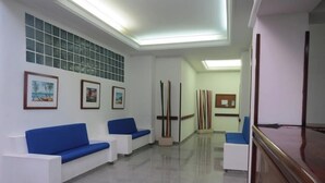 Un'area reception con divani bianchi, opere d'arte incorniciate alle pareti e un banco reception in legno.